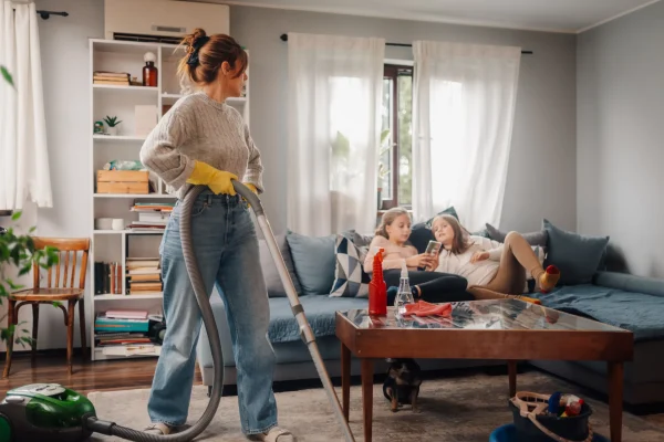 mother-vacuuming-living-room-while-daughters-relax-2025-08-27-10-05-47-utc_11zon